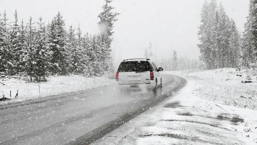 Auto ziemas ceļā sniegotā mežā, atstājot sniega pēdas un izraisot sniegputeni.