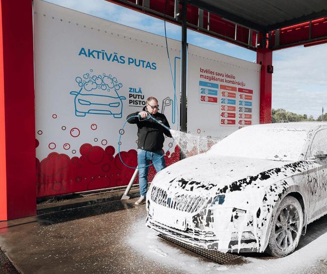 Vīrietis mazgā auto ar putām PUTO pašapkalpošanās automazgātavā.