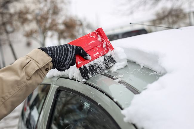 Removing snow from a car roof with a brush in winter conditions