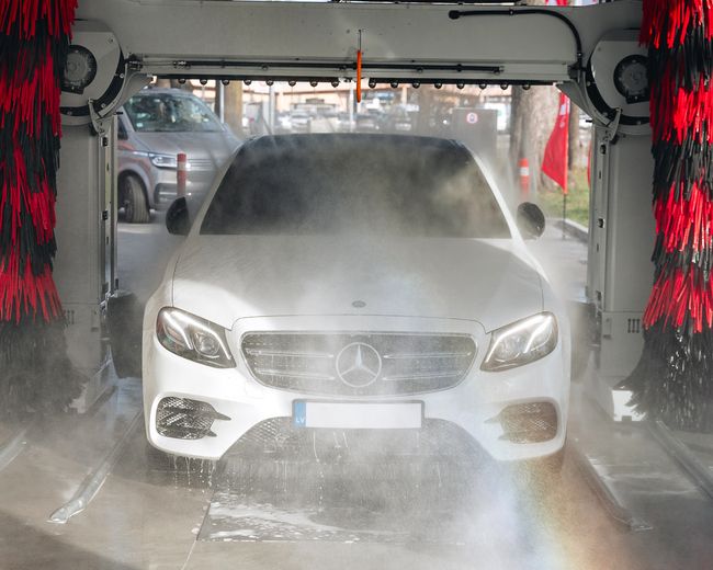 Balts auto automātiskajā mazgātavā, ieskauts ūdens miglā.