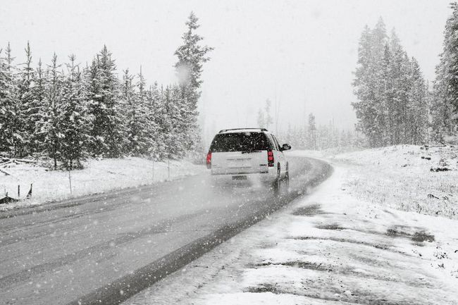 Auto ziemas ceļā sniegotā mežā, atstājot sniega pēdas un izraisot sniegputeni.