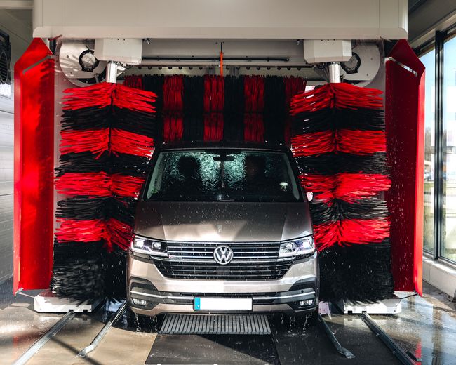 Pelēka mašīna automazgātavā starp lielām birstēm.