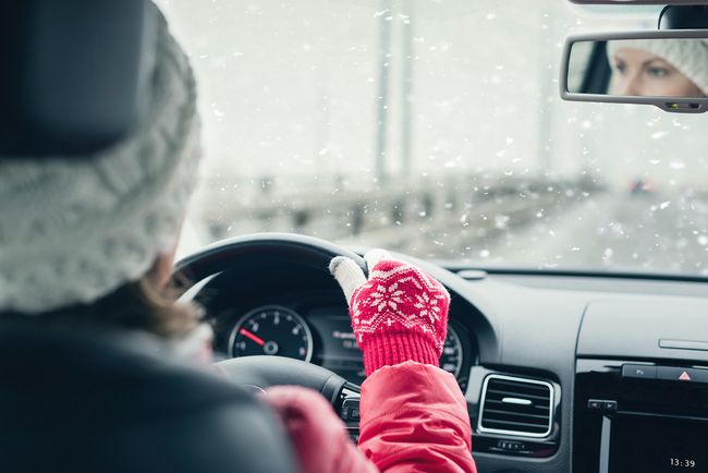 Driver wearing gloves holding the steering wheel while driving in snowy winter conditions with poor visibility