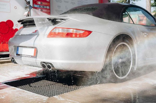 Car being washed with a high-pressure washer at PUTO self-service car wash during summer.