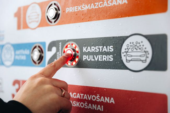 Pirksts nospiež karstā pulvera programmas pogu PUTO pašapkalpošanās automazgātavā