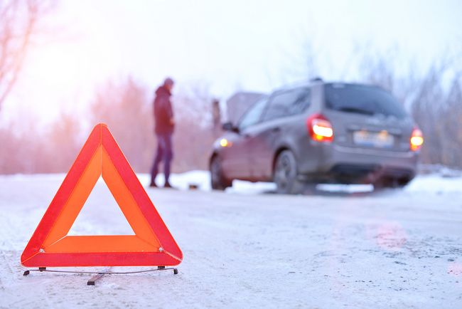 Warning triangle on a snowy road next to a stopped car in winter conditions