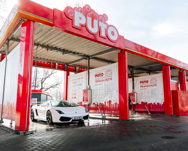 Automazgātava PUTO, sarkanā un baltā krāsas pašapkalpošanās boksā iedzīta balta sporta mašīna