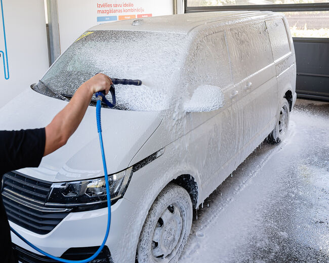 Balts VW Transporter mikroautobuss tiek mazgāts ar aktīvajām putām PUTO pašapkalpošanās mazgātavas boksā