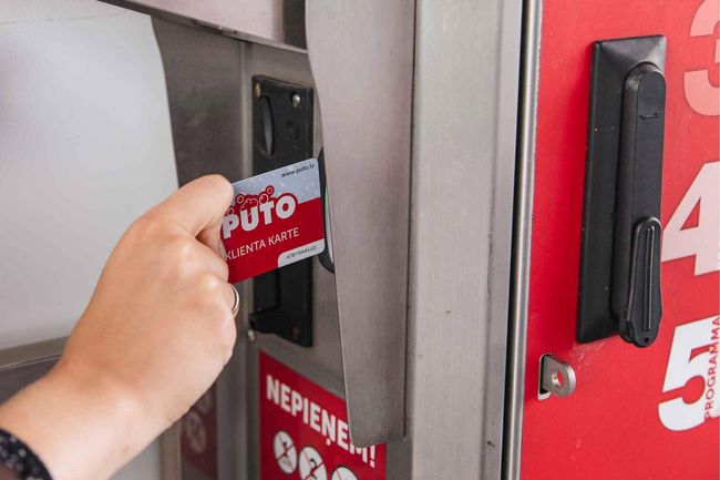 Hand inserting a PUTO client card into a payment machine slot.