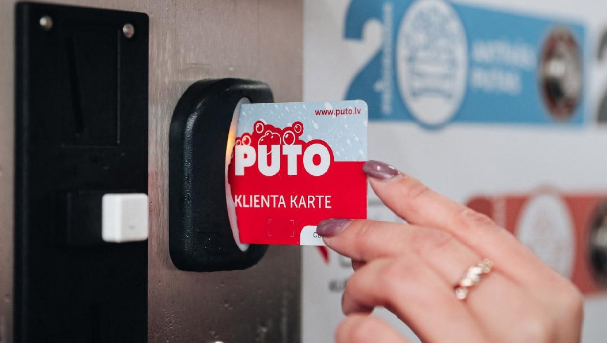 Hand holding a PUTO client card at a payment machine sensor.