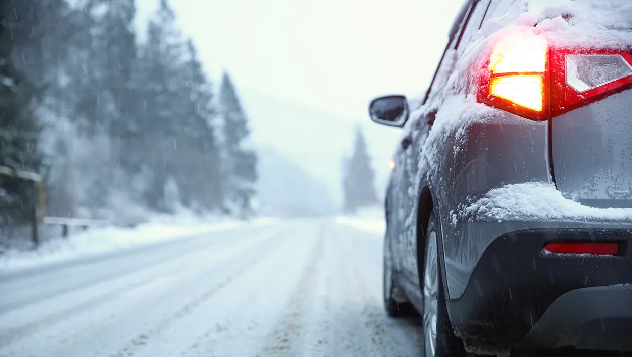 Automašīna uz sniegota ziemas ceļa ar iedegtiem aizmugures lukturiem un sliktu redzamību