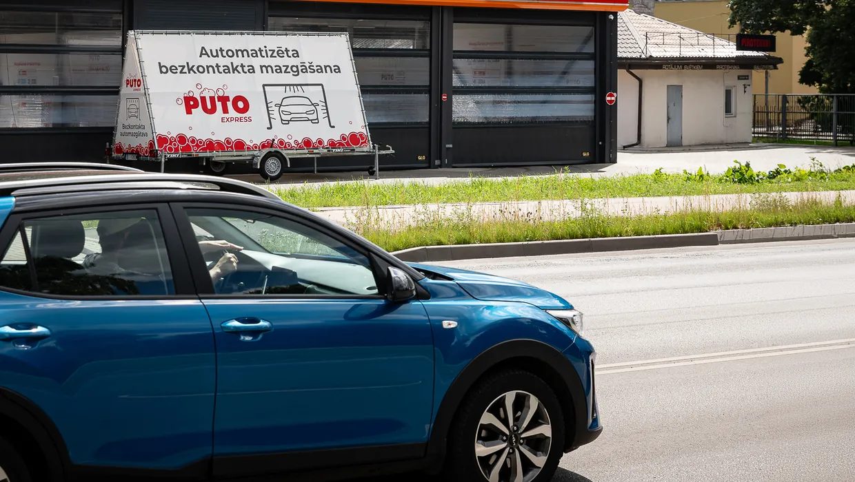 Zils auto brauc garām PUTO automazgātavai ar PUTO Express bezkontakta mazgāšanas reklāmas baneri
