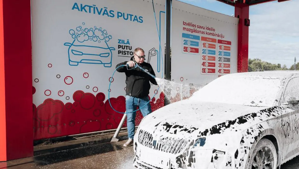 Мужчина моет автомобиль пеной на самообслуживаемой автомойке PUTO.