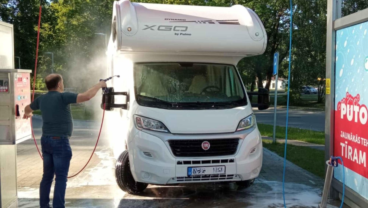 Man washing a white camper van at the PUTO car wash using a high-pressure water spray.