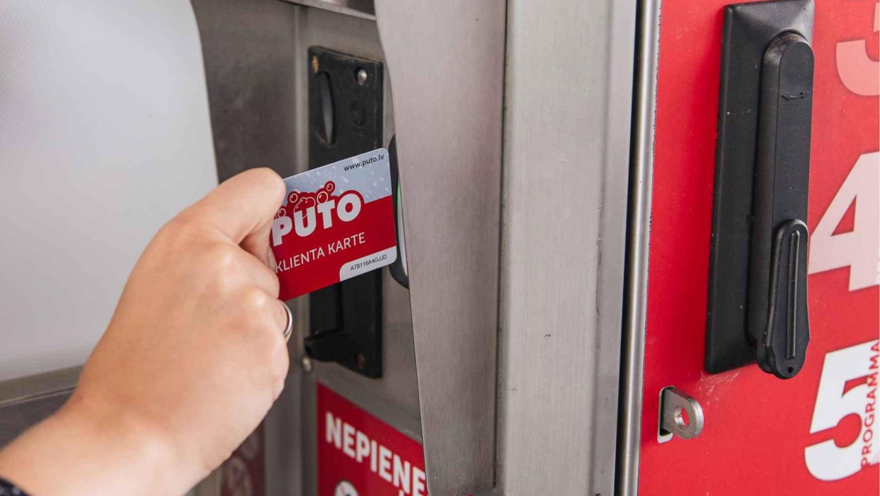 Hand inserting a PUTO client card into a payment machine slot.