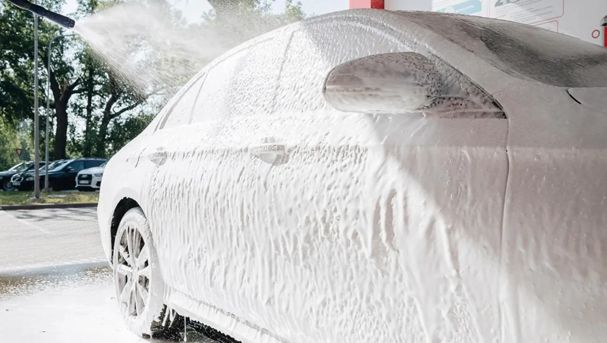 Car at the PUTO car wash, covered in foam and being washed with a high-pressure water spray.